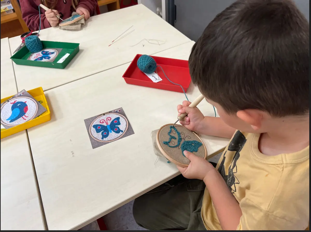 Élève de primaire réalisant un papillon en punch needle lors d'un atelier en classe